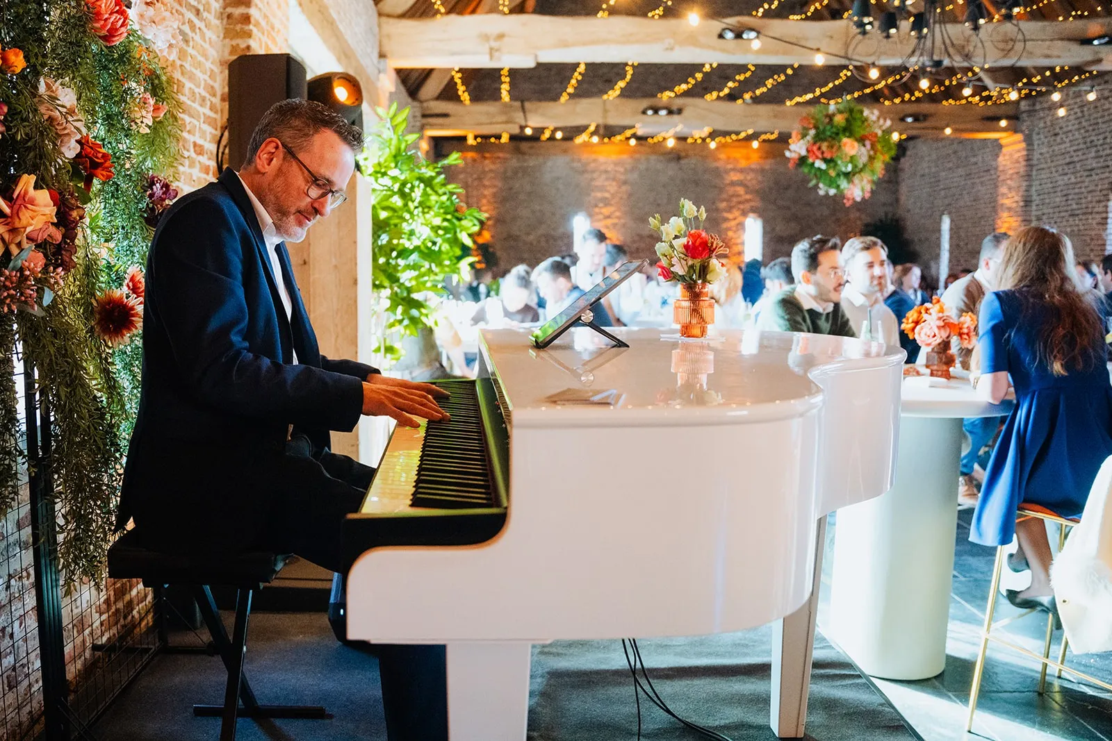 Rik Deckers aan een witte vleugel tijdens een event, gasten op de achtergrond
